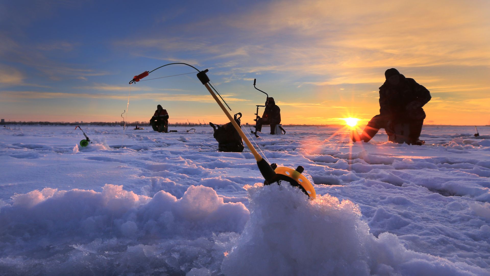 Vissers doen aan ijsvissen bij zonsondergang.
