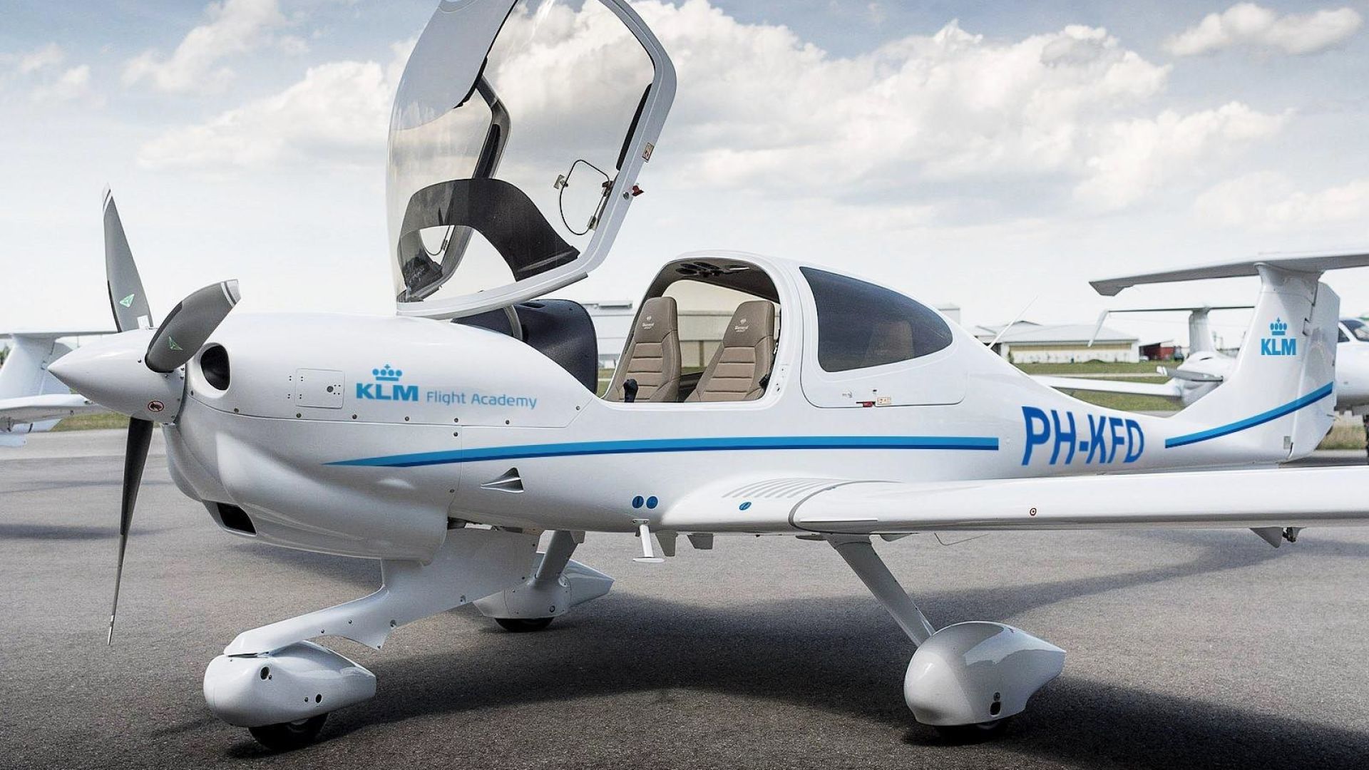 Een klein sportvliegtuig met open cockpit op een vliegveld.