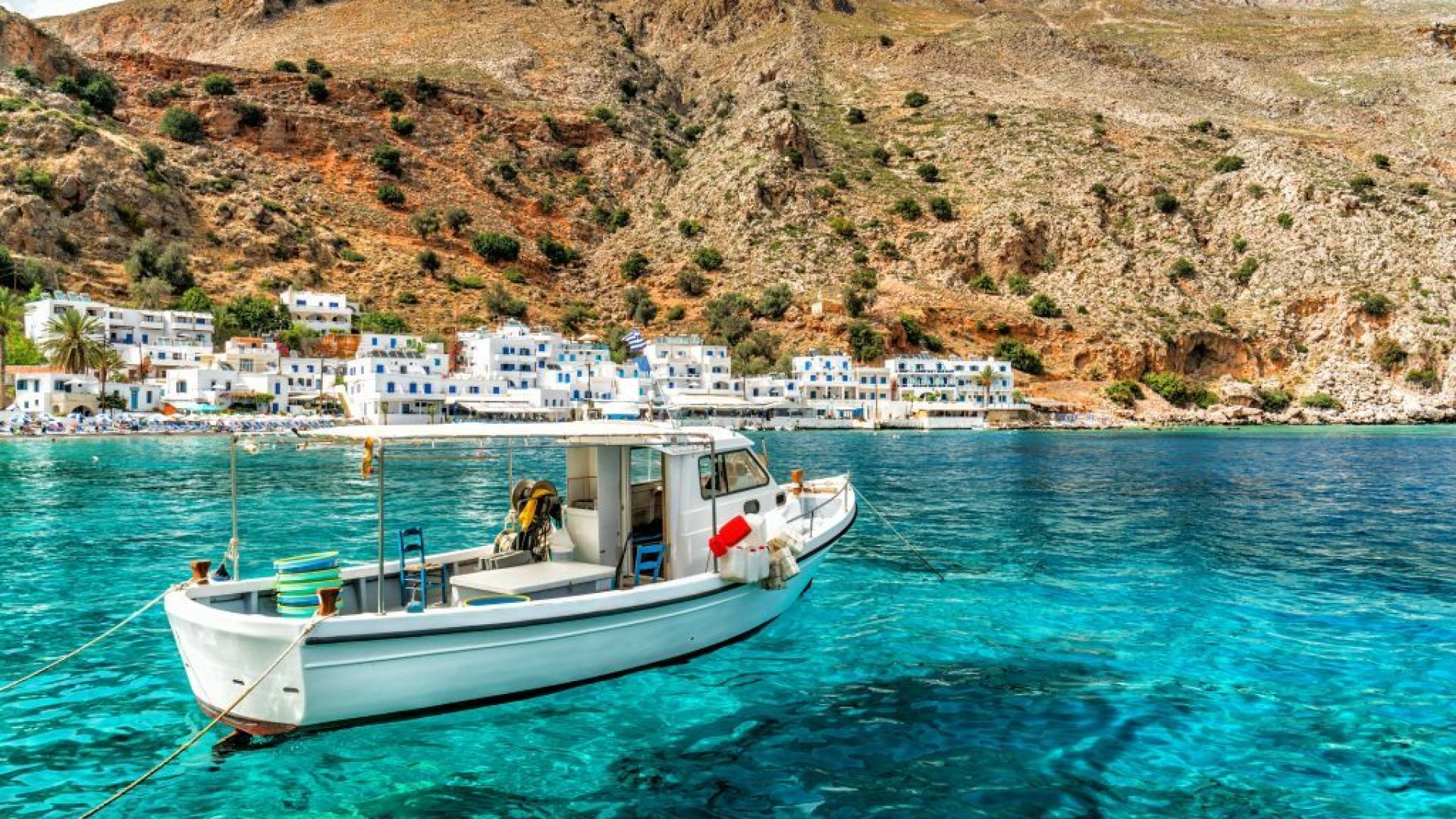 Een vissersboot dobbert op helderblauw water bij een schilderachtig kustdorp.