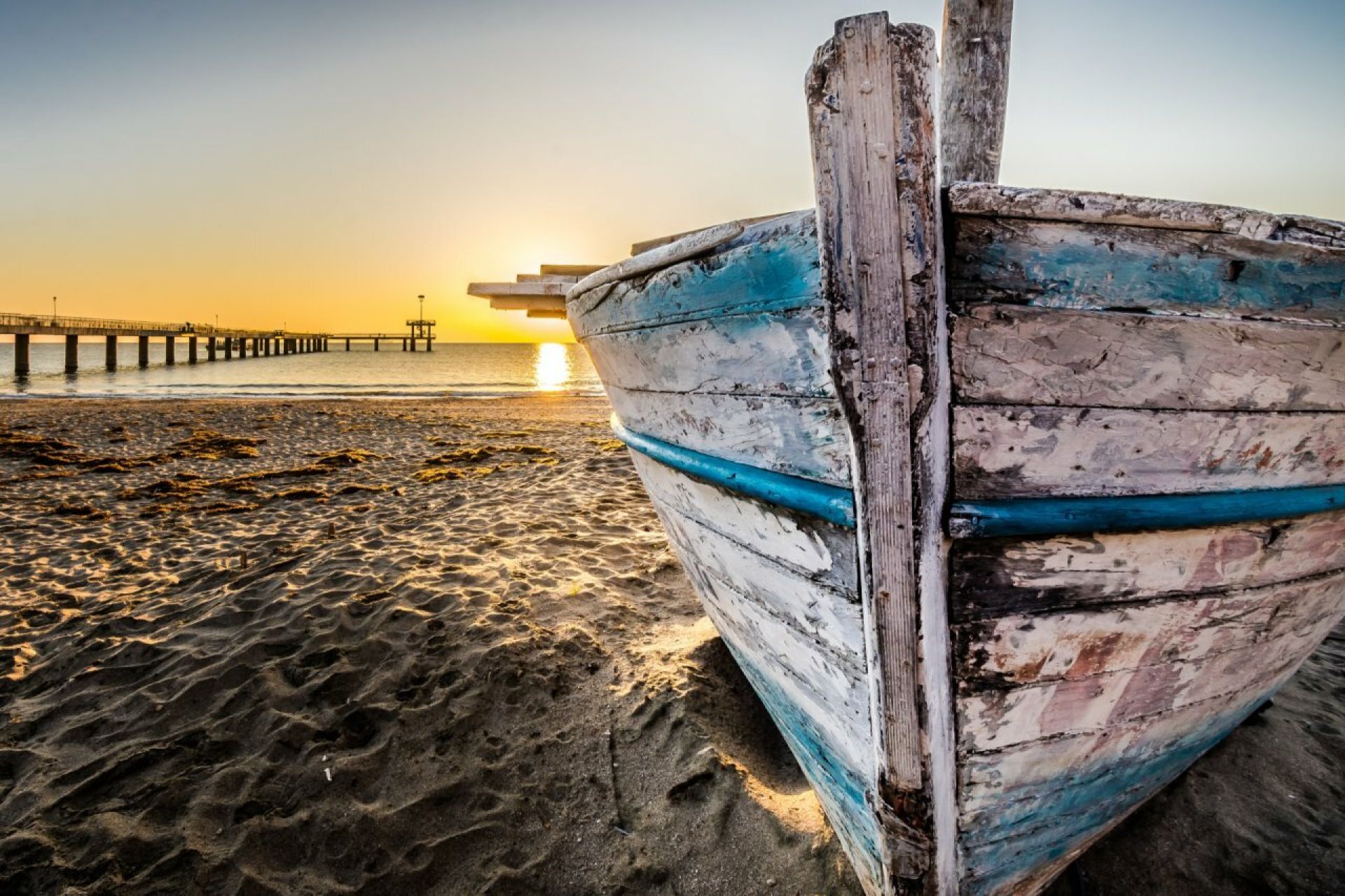 Een verweerde houten boot op het strand bij zonsondergang.