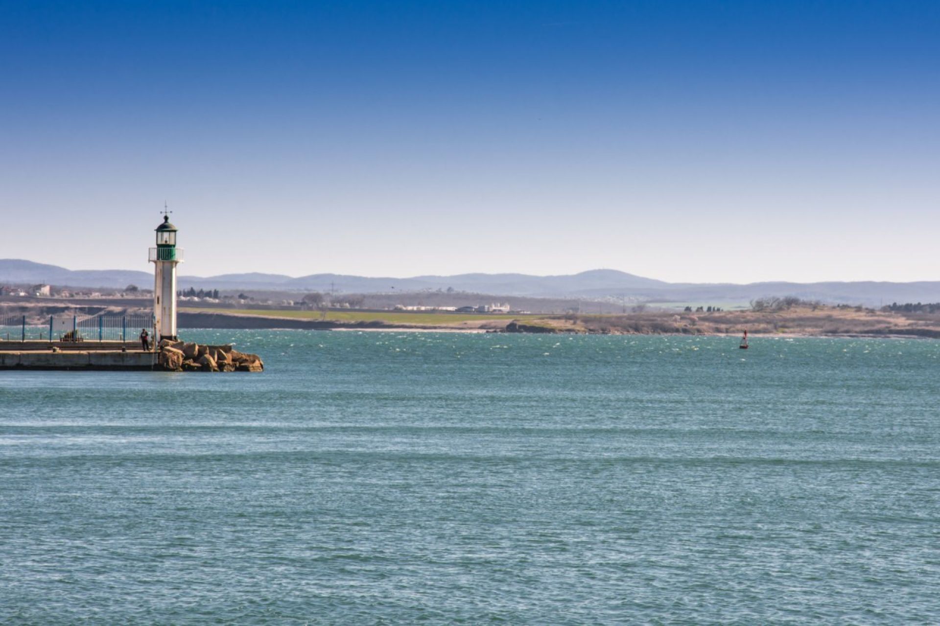 Vuurtoren aan de kust met een rustige zee en heuvels op de achtergrond.