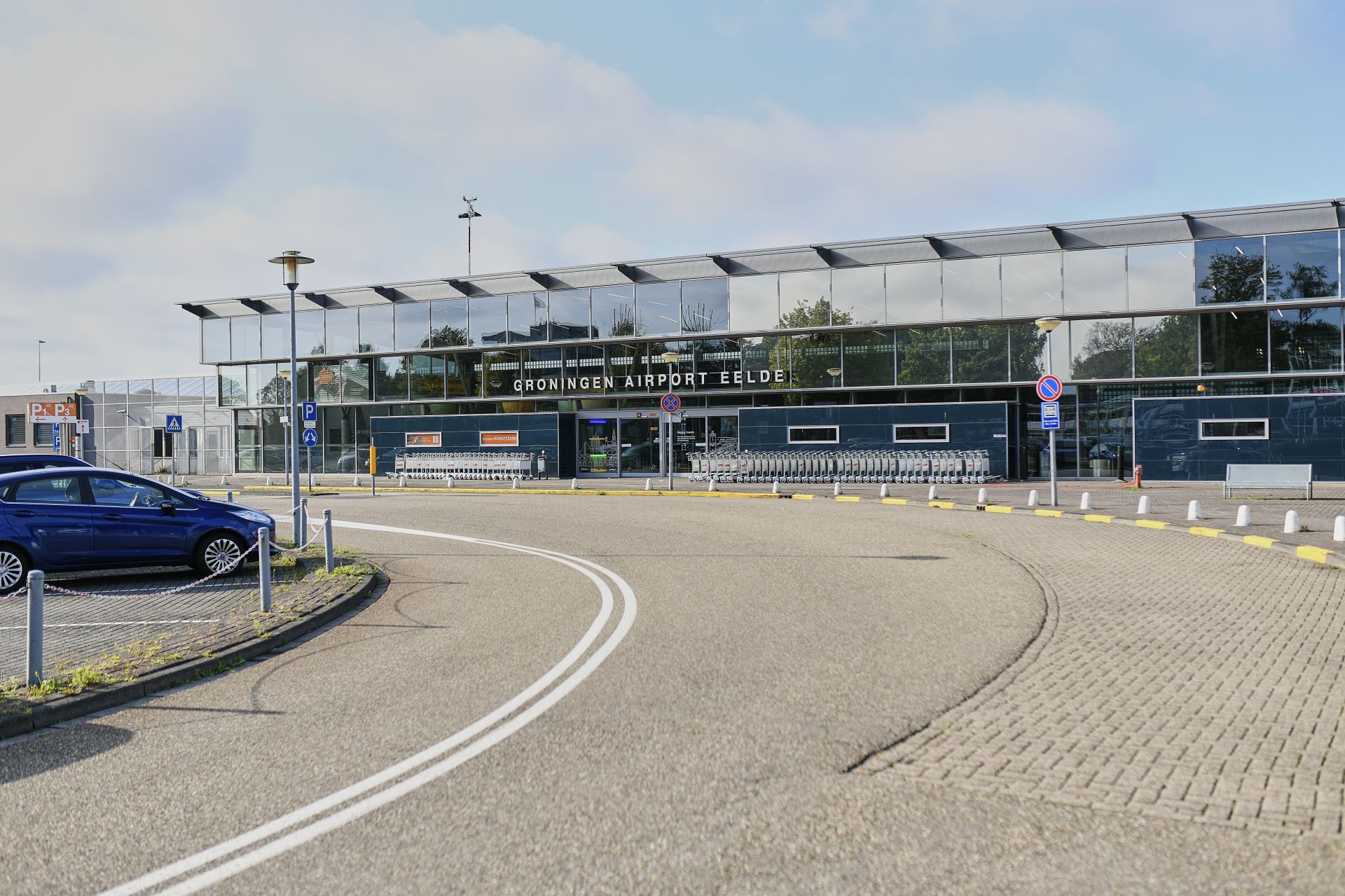 Buitenkant van een luchthaven met een weg en geparkeerde auto.